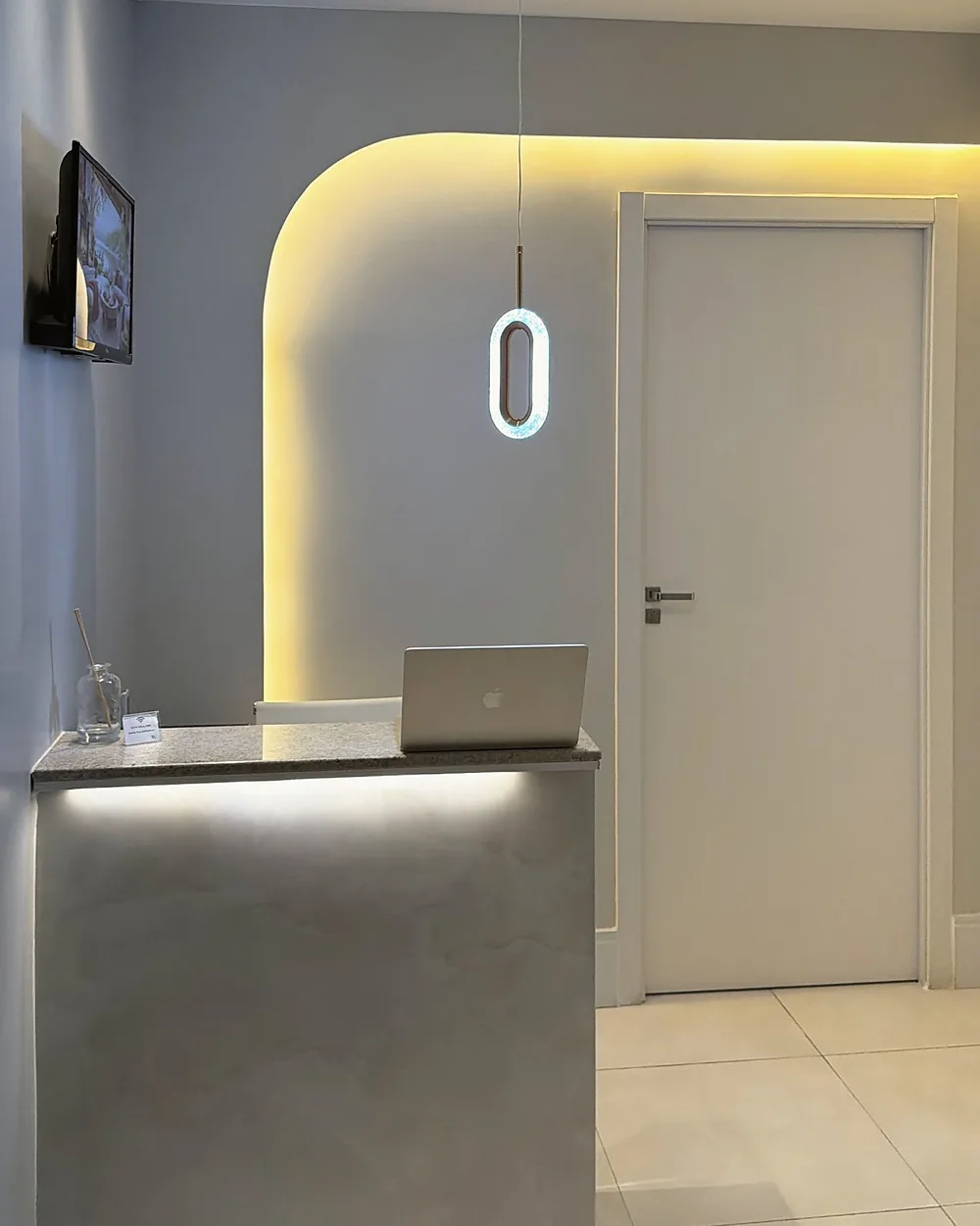 Recepção da sala 1905, com balcão claro e parede em arco iluminada por luz dourada